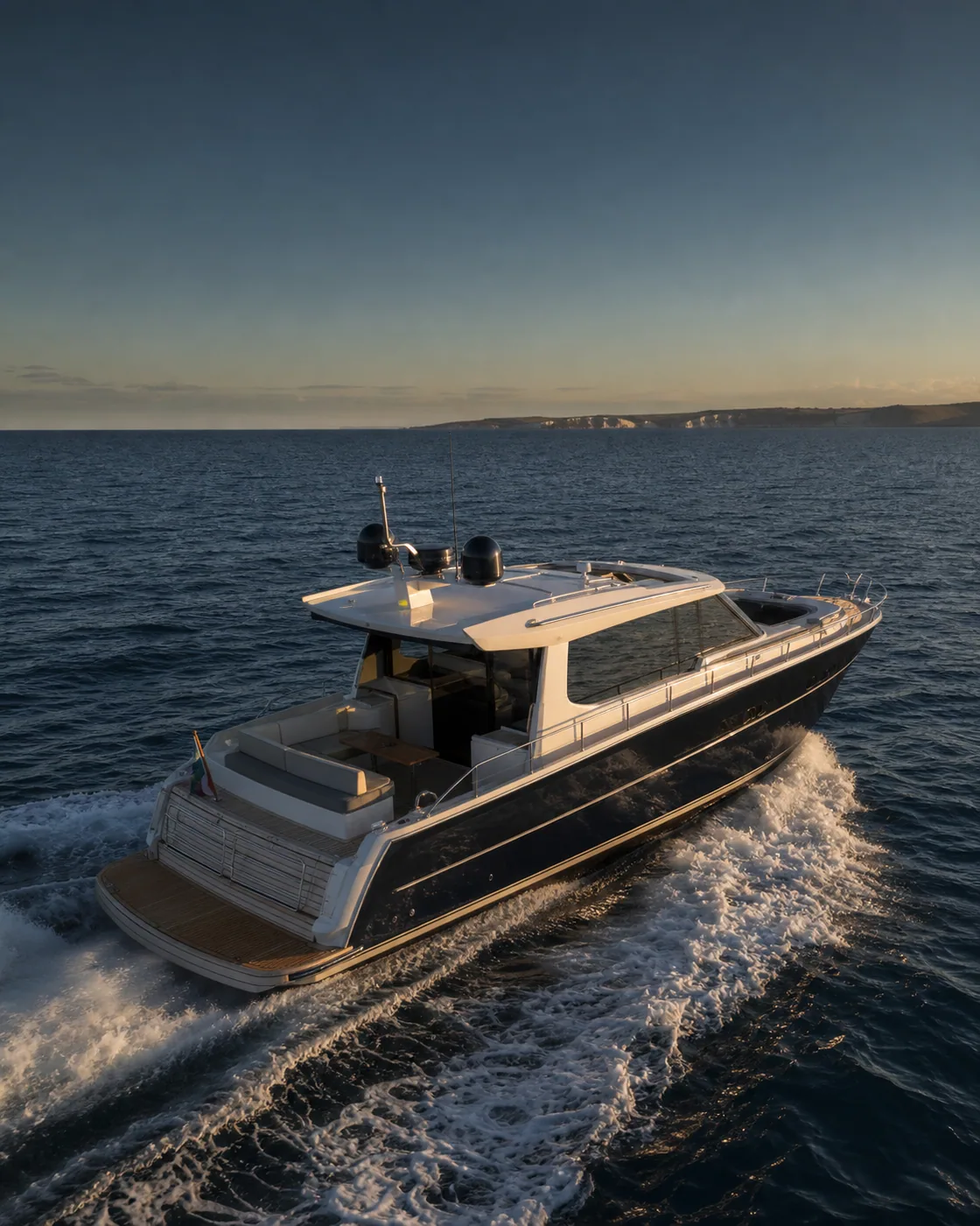 Modern motor yacht crossing deep blue coastal water at golden hour